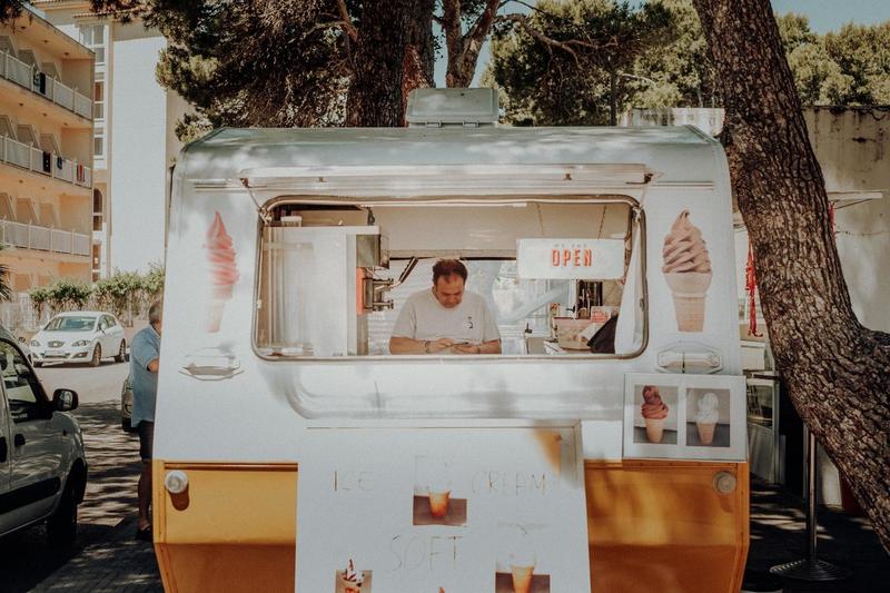 A Man in a White Food Truck Selling Ice Cream on the Side of a Street