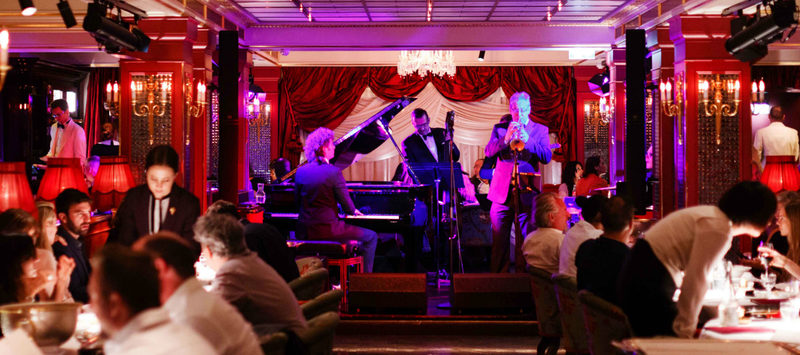 Busy Restaurant With a Band Playing on the Stage, Dark Setting and Candles on All the Tables